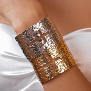 Detail of wide hammered metal bangles with cross cutout on white silk fabric