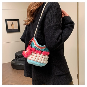 Detail view of pink and blue crochet bucket bag with pearl strap worn by a model