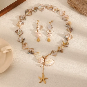 Seashell necklace and earrings set with pearls and gold metal on beige fabric
