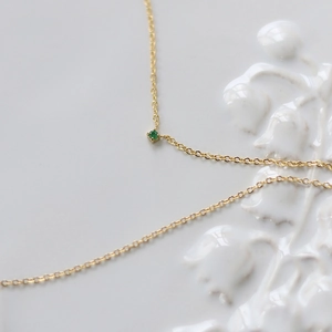 Close-up of gold titanium crescent moon necklace with a green zircon on ceramic