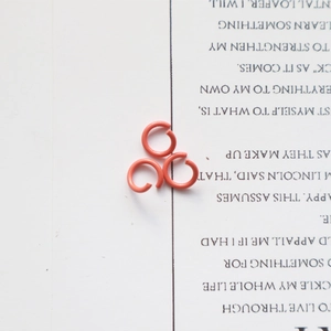 Detailed view of three vibrant orange lacquered metal jump rings for DIY jewelry making