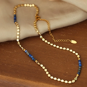 Golden titanium steel beaded necklace with blue natural stones on a silk fabric background
