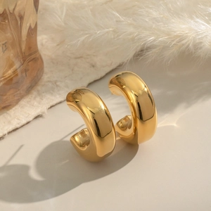 Vue détaillée des boucles d'oreilles créoles dorées 18K sur un décor esthétique chaud
