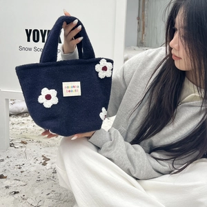 Close-up of a navy blue plush handbag featuring three white floral 3D appliques