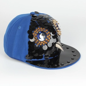 Close-up of owl hip-hop hat with sequins, golden spikes, and blue gem eye detail