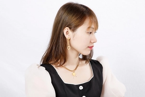 Close-up of a woman wearing a gold heart pendant necklace and matching drop earrings