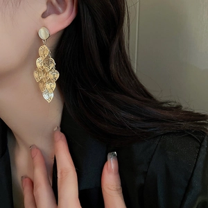 Detail view of gold leaf tassel earrings with cat-eye stone on a female model