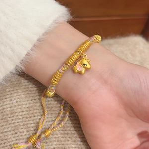 Detailed close-up of woven red rope bracelet with golden unicorn charm on woman's wrist