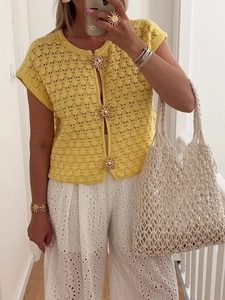 Close-up of yellow crochet knit cardigan featuring golden sunflower-shaped buttons