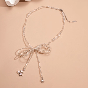 Beaded necklace with silver bow, heart and pink crystal pendants on brown backdrop