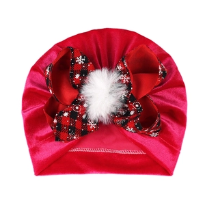 Close-up of red velvet baby turban hat with festive plaid bow and white pompom detail