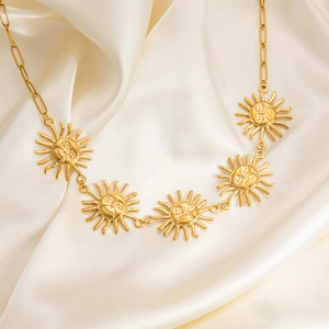 Detail of gold sun face pendants on a stainless steel necklace over beige silk fabric