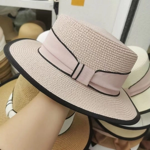 Handheld photo of a beige flat top straw boater hat with black trim and ribbon bow