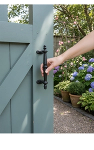 Vintage black cast iron handle shown on a rustic garden gate with a hand for scale