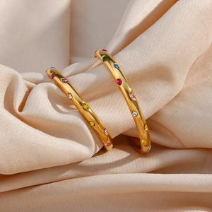 Macro detail of 18K gold plated hoop earrings with multi-colored zircon stones on silk