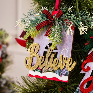 Macro view of wooden house ornament with glittery 'Believe' text and plaid bow
