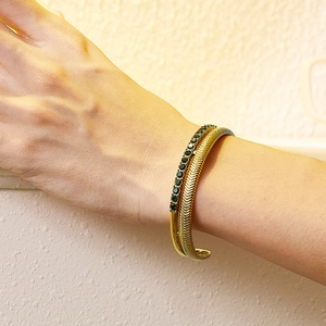 Detail of gold double-layer open bangle with green gemstones and fishbone texture
