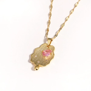 Detail of gold pendant necklace with pear-shaped pink stone and cubic zirconia inlay