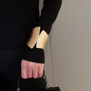Macro detail of a wide gold-toned irregular cuff bracelet worn over a black sweater sleeve