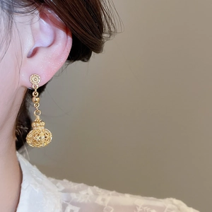 Close-up of model wearing gold hollow lantern pendant earrings with intricate texture