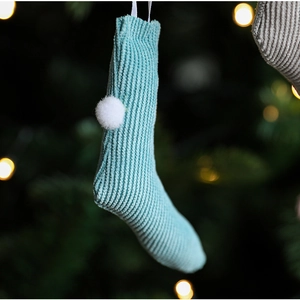 Macro shot of light blue knit Christmas stocking with white pom-pom on a festive tree