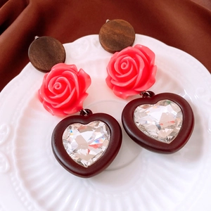 Macro detail of vintage heart earrings with red resin roses and crystal on a white plate