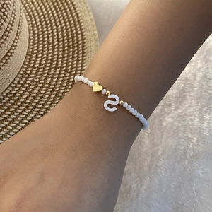 Detail of white beaded bracelet with letter S pendant and gold heart on female wrist