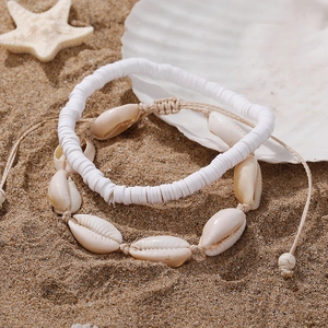 Detail view of woven shell anklet set with white beads on a sandy beach setting