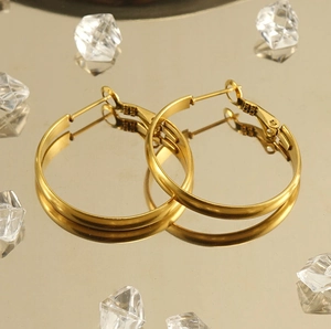 Close-up of polished gold hoop earrings on a reflective champagne surface with ice crystals