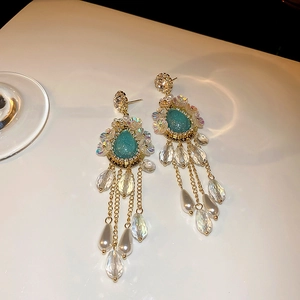 Detail view of golden long tassel earrings with teal gems and white floral accents