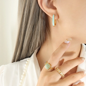 Elegant U-shaped light blue enamel earrings and green gemstone rings on model