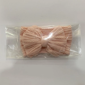 Pink textured knit baby headband with a large bow in transparent packaging on white