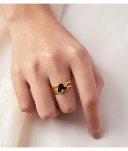 Détail d'une bague multicouche dorée avec un cœur en émail noir portée à la main