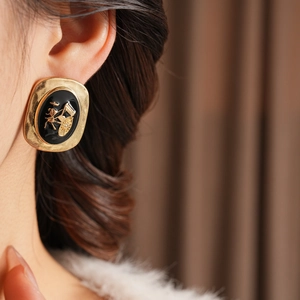 Detail of vintage oval earrings with gold metal frame and black enamel carriage relief