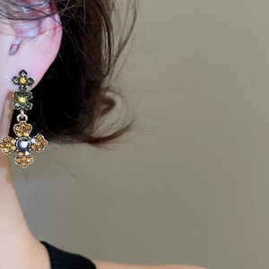 Macro shot of vintage floral drop earrings with green and yellow gems on a model