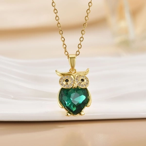 Macro detail of golden owl pendant with a heart-shaped green crystal on a gold chain