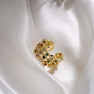 Macro detail of gold ear cuff with colorful cubic zirconia on white silk background