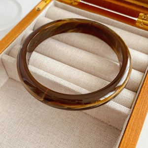 Detailed view of an amber tortoise shell resin bangle resting in a wooden jewelry box