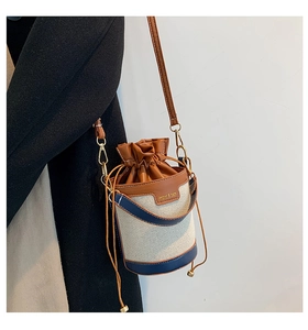 Detail of canvas bucket bag with brown leather trim and drawstring closure on model