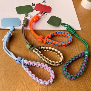 Adjustable braided paracord phone wrist strap in multiple colors on a wooden surface