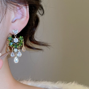 Close-up of gold drop tassel earrings with green crystals worn by a female model