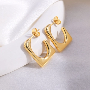 Detailed close-up of gold square U-shaped earrings resting on elegant white silk and ceramic