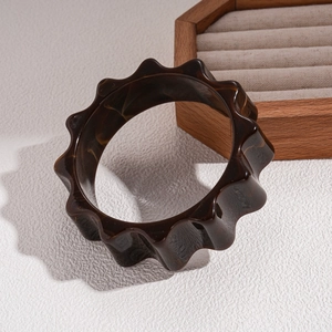Close-up of a wide acrylic bangle featuring dark tortoise shell pattern and wavy edges