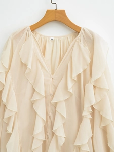 Detail of elegant beige V-neck shirt featuring layered ruffles and delicate buttons