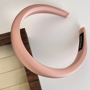 Detailed macro view of pink satin padded headband featuring a handmade label on white background