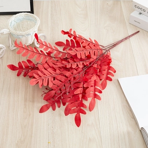 Detail shot of red artificial fern foliage with white woven tricycle on wooden floor