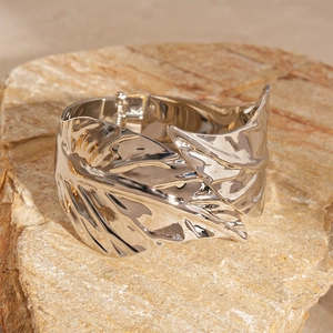 Detail shot of a polished silver leaf-shaped open cuff bracelet on a natural stone surface