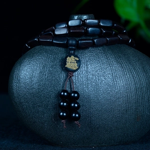 Dark wood prayer bead bracelet with gold Chinese engraving on a matte ceramic jar