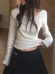 Détail d'un haut blanc à manches longues avec motif à pois noirs porté par un mannequin