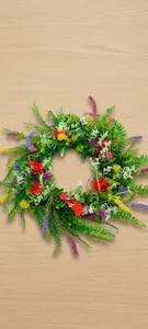 Close-up of vibrant artificial wildflower wreath with colorful ranunculus and green leaves